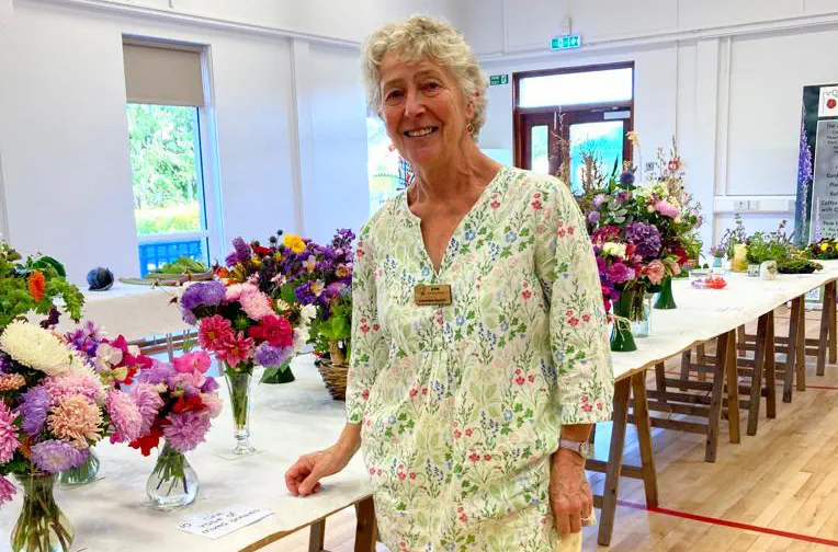 Caroline, Chair of the Ayton Gardening Society, standing in front of the table displaying the floral entries